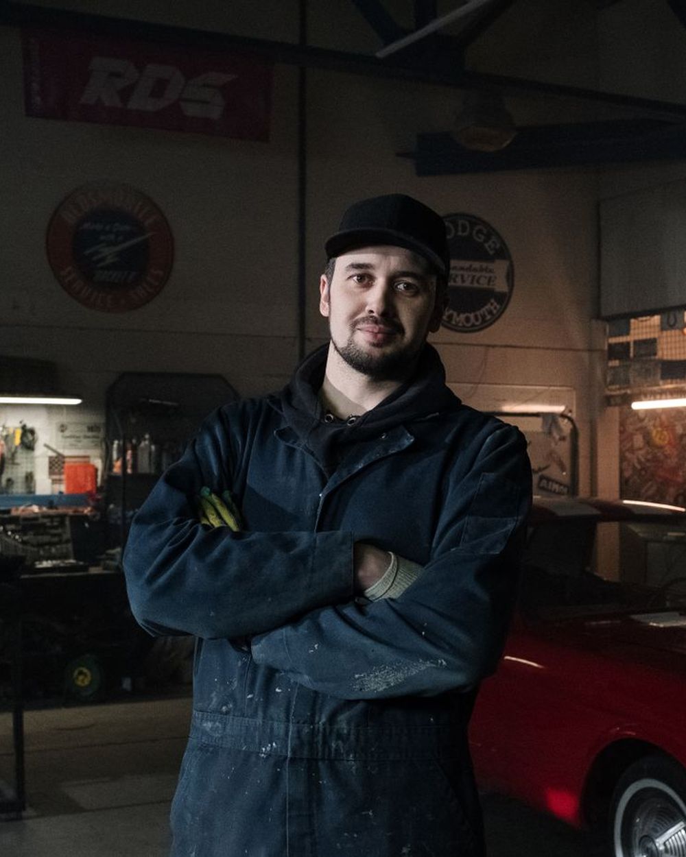 Technician standing in the garage with arms crossed, a classic car behind him